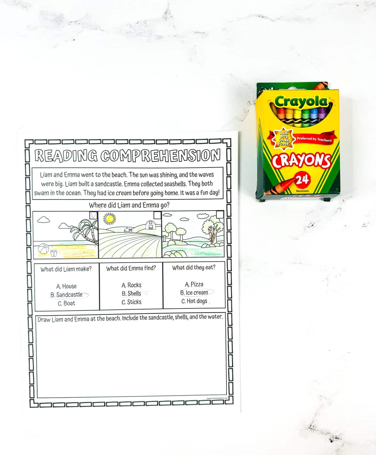 A children’s summer reading comprehension worksheet featuring a story about Liam and Emma’s beach day. The worksheet includes three answer boxes with questions about the story—where they went, what they made or found, and what they ate—and ends with a drawing prompt asking kids to illustrate the beach scene including the sandcastle, shells, and water. A box of 24 Crayola crayons sits to the right on a white marble background.