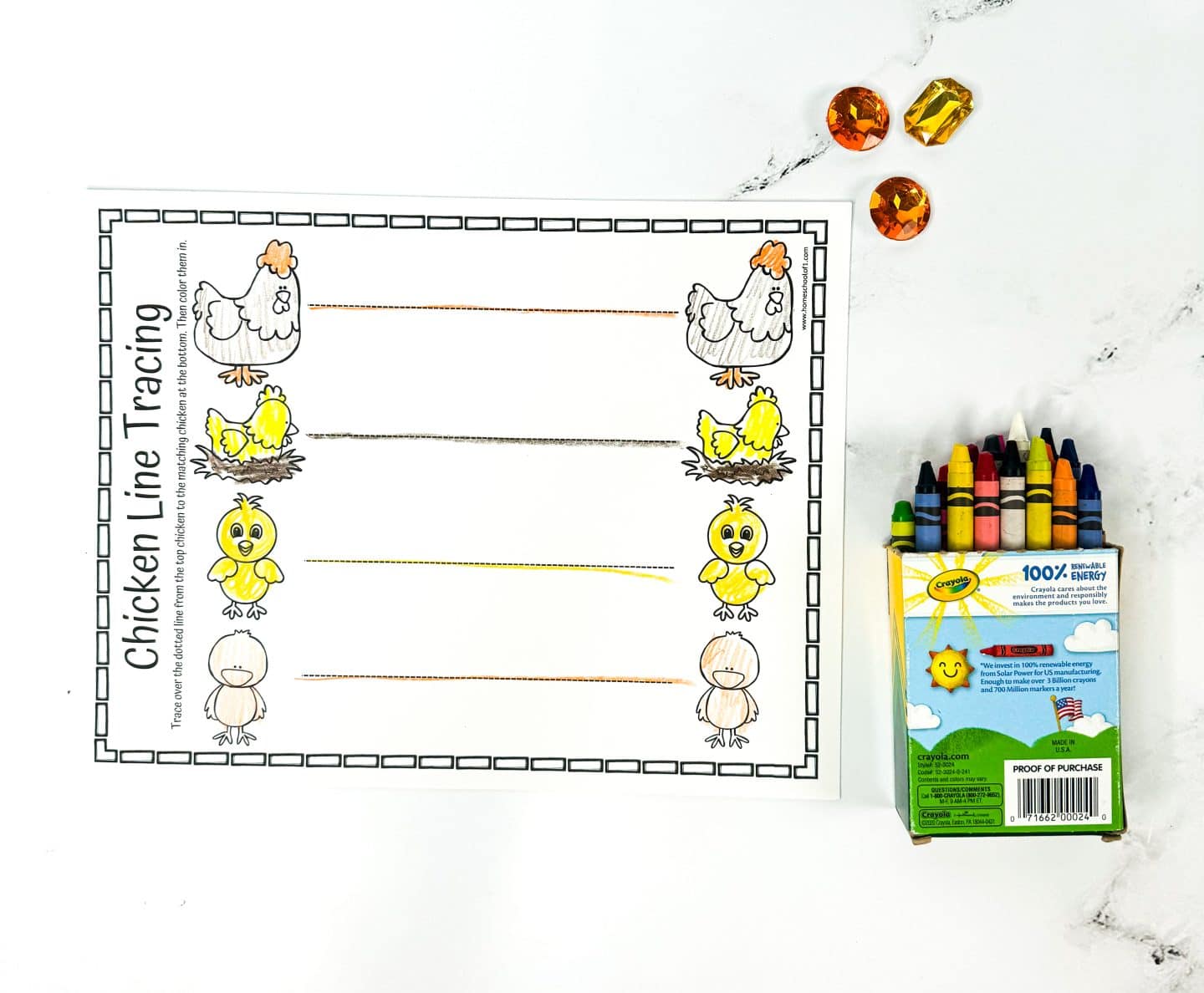 A worksheet titled Chicken Line Tracing featuring lines with images of chicks at the start and end of each line, guiding the tracing. Nearby, there are crayons and three amber-colored gems on a white background.

