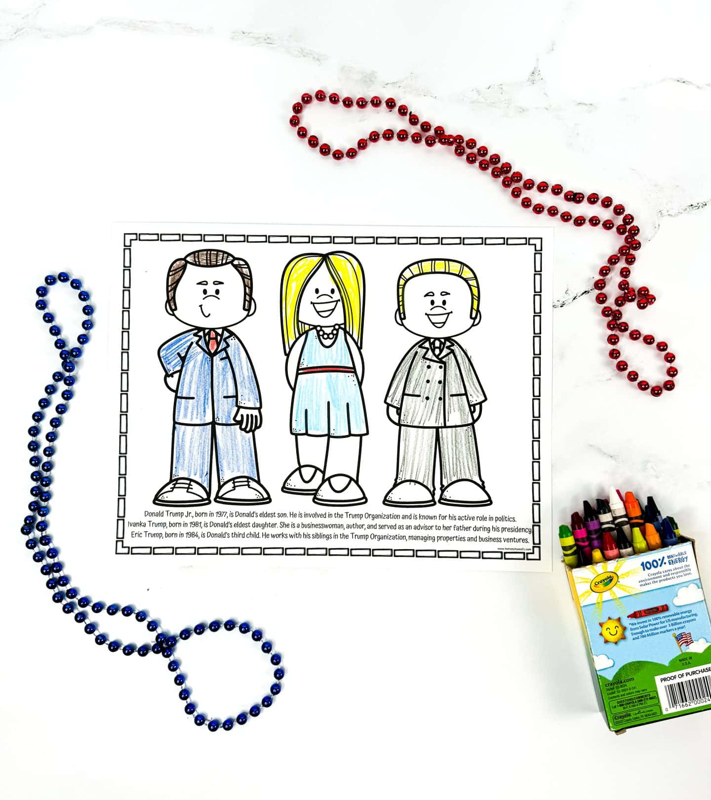 A completed coloring worksheet shows cartoon versions of Donald Trump Jr., Ivanka Trump, and Eric Trump, each colored with crayons and standing side by side. Below the drawings is a short biography of each sibling, describing their roles in the Trump Organization and public life. The page is surrounded by red and blue bead necklaces and a box of Crayola crayons.