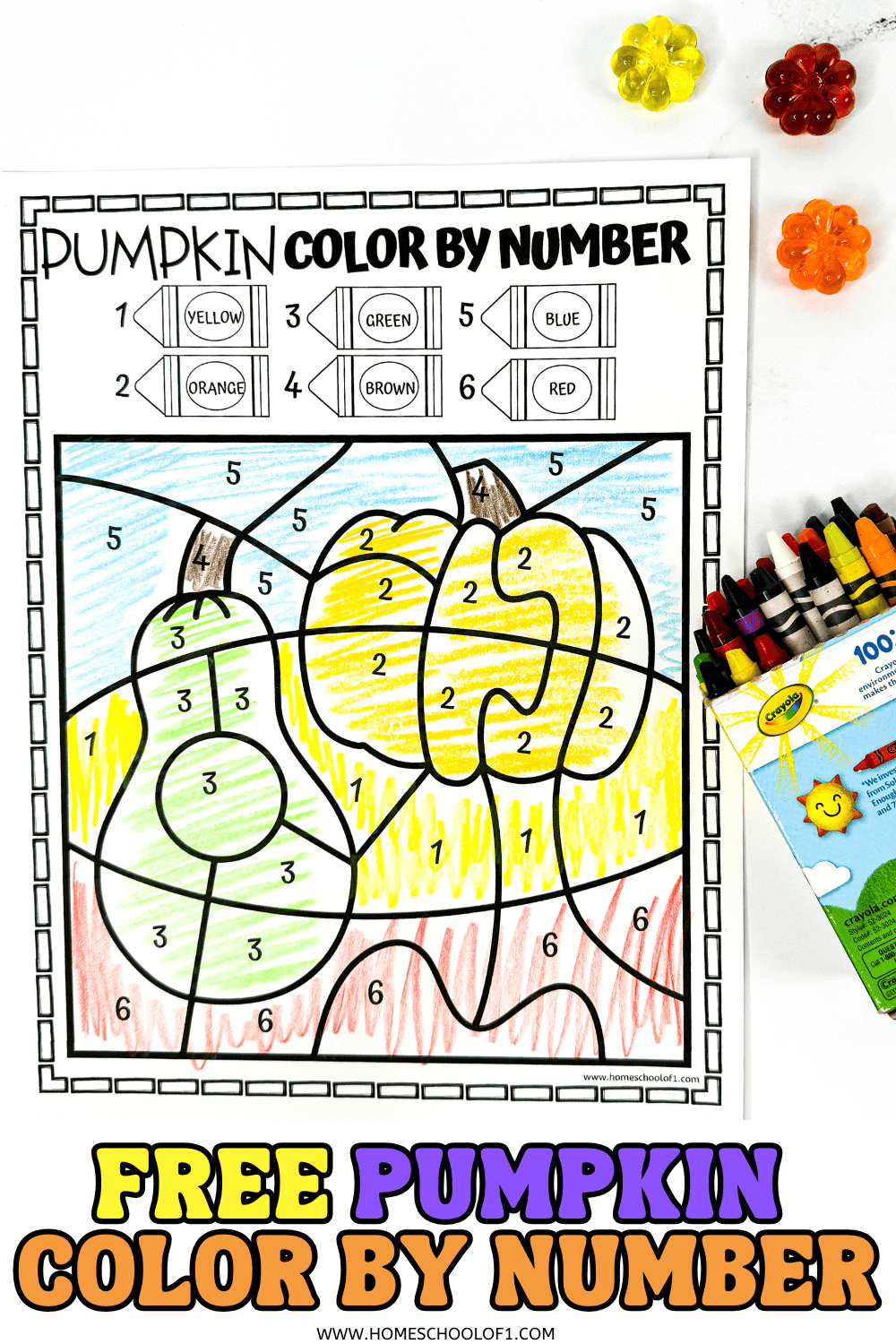 Pumpkin color-by-number page mostly colored in yellow and green, next to a crayon box and small fall decor.