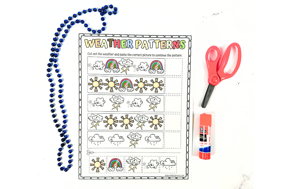 Black-and-white printable worksheet titled "Weather Patterns," featuring rows of weather icons like sunshine, clouds, rain, lightning, and rainbows, with blank spaces to complete the sequences. Instructions at the top prompt kids to cut and paste the correct weather image to finish each pattern. A pink pair of scissors, glue stick, and blue bead necklace are arranged around the worksheet.
