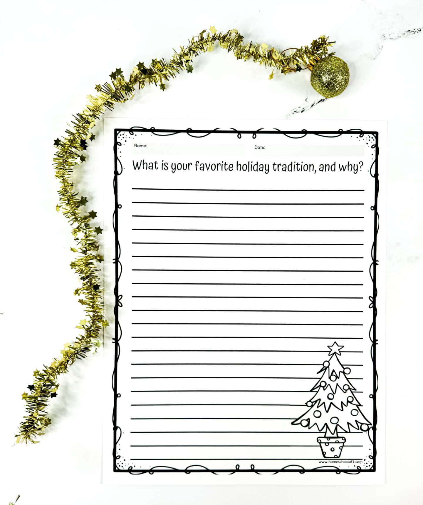 A festive writing prompt worksheet titled “What is your favorite holiday tradition, and why?” includes wide-ruled lines for student responses and a decorative Christmas tree illustration in the bottom corner. The page features a playful black border and is surrounded by gold tinsel and a glittery ornament, creating a cheerful holiday atmosphere.

