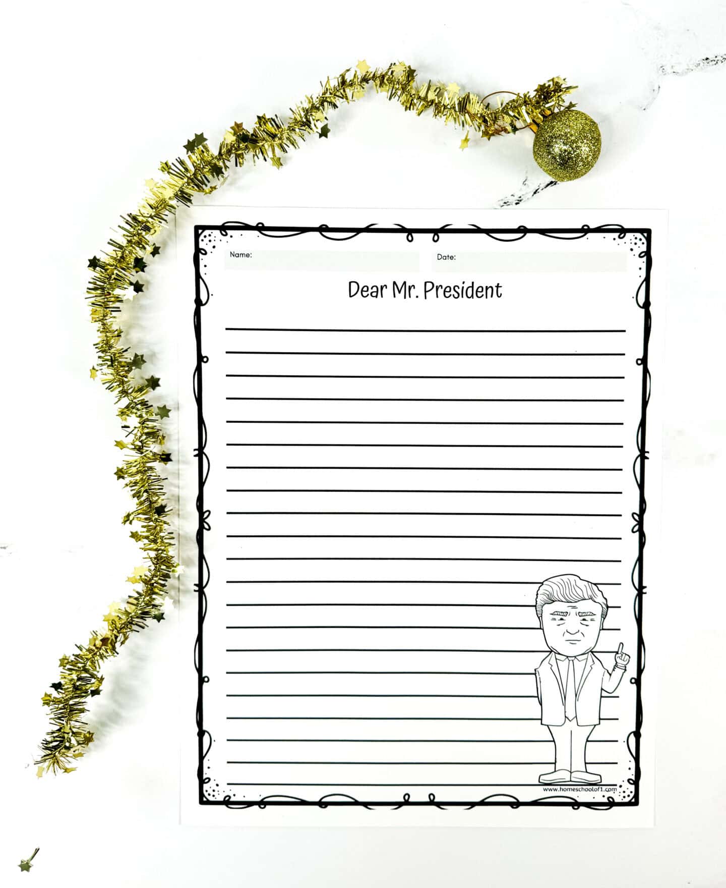 A printable writing prompt page titled “Dear Mr. President” features lined space for kids to write a letter, with a black-and-white cartoon illustration of a man in a suit pointing upward in the bottom corner. The worksheet has a decorative border and is laid on a white background with gold tinsel and a glittery ornament nearby, adding a festive holiday touch.

