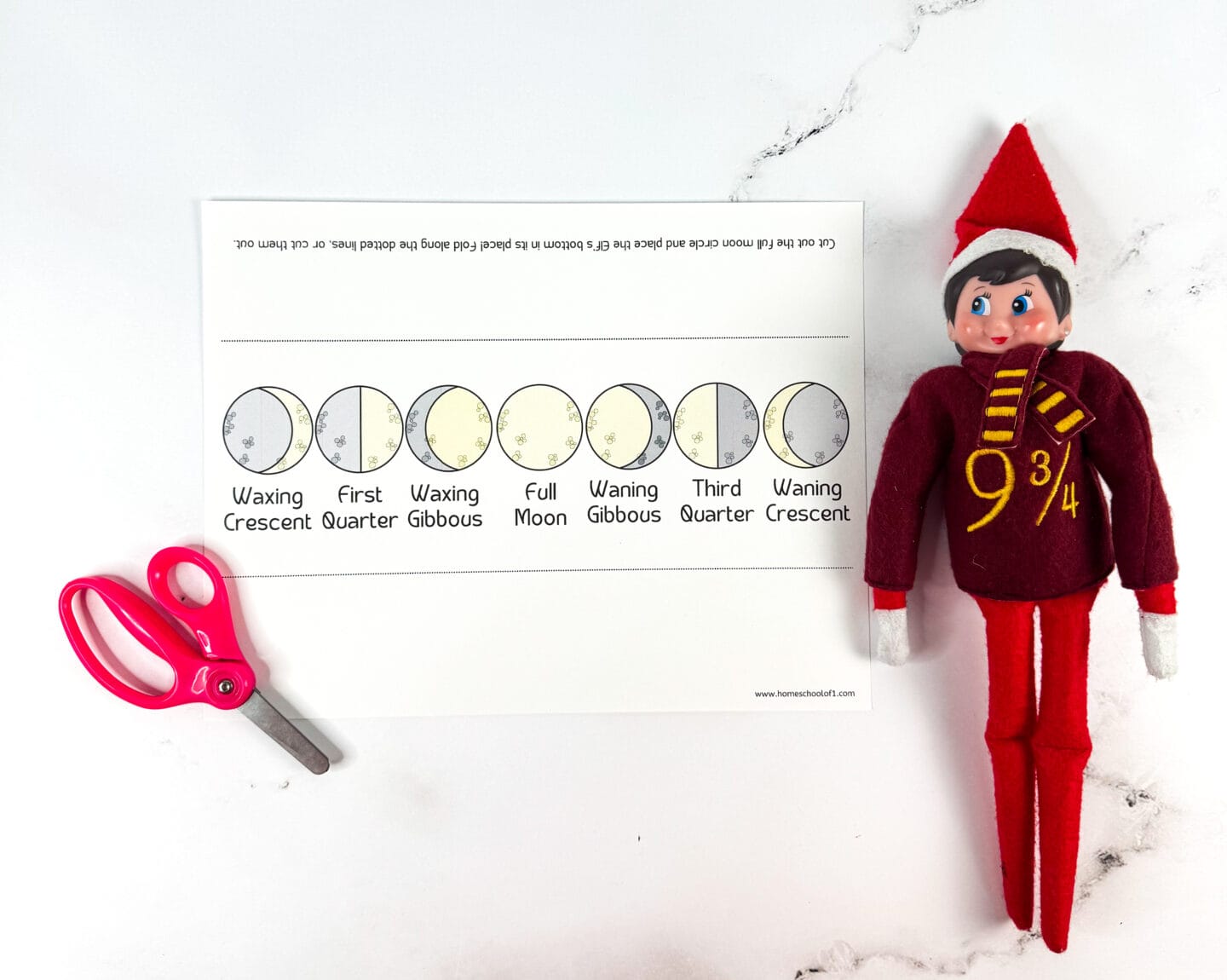 A printable moon phases chart laid flat on a white surface, showing all eight lunar phases from Waxing Crescent to Waning Crescent. A red Elf on the Shelf doll wearing a “9¾” Harry Potter-themed sweater is placed beside the chart, with a pair of pink scissors positioned to the left. The setup suggests a fun science-themed Elf on the Shelf activity.

