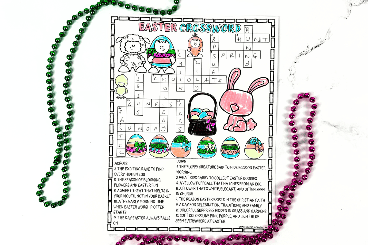 Easter-themed kids' crossword puzzle partially colored in, featuring spring illustrations like a pink bunny, Easter eggs, a lamb, a chick, and an egg basket. The crossword is filled out with words like “bunny,” “chocolate,” “sunrise,” “Sunday,” and “pastel,” all based on Easter-related clues. The page is surrounded by green and pink beaded necklaces on a white marble surface.