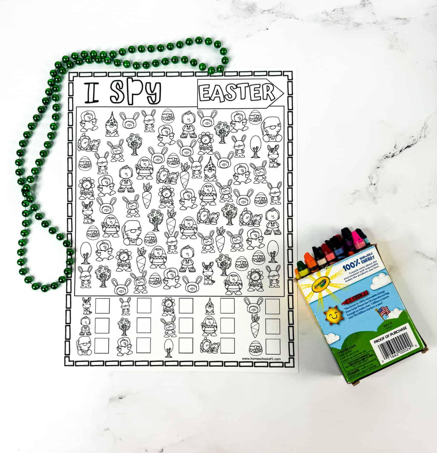Black-and-white "I Spy Easter" worksheet filled with fun illustrations like chicks, bunnies, carrots, eggs, and kids in costumes, ready to be colored. The page is shown with a string of green beads and a box of crayons on a white background.