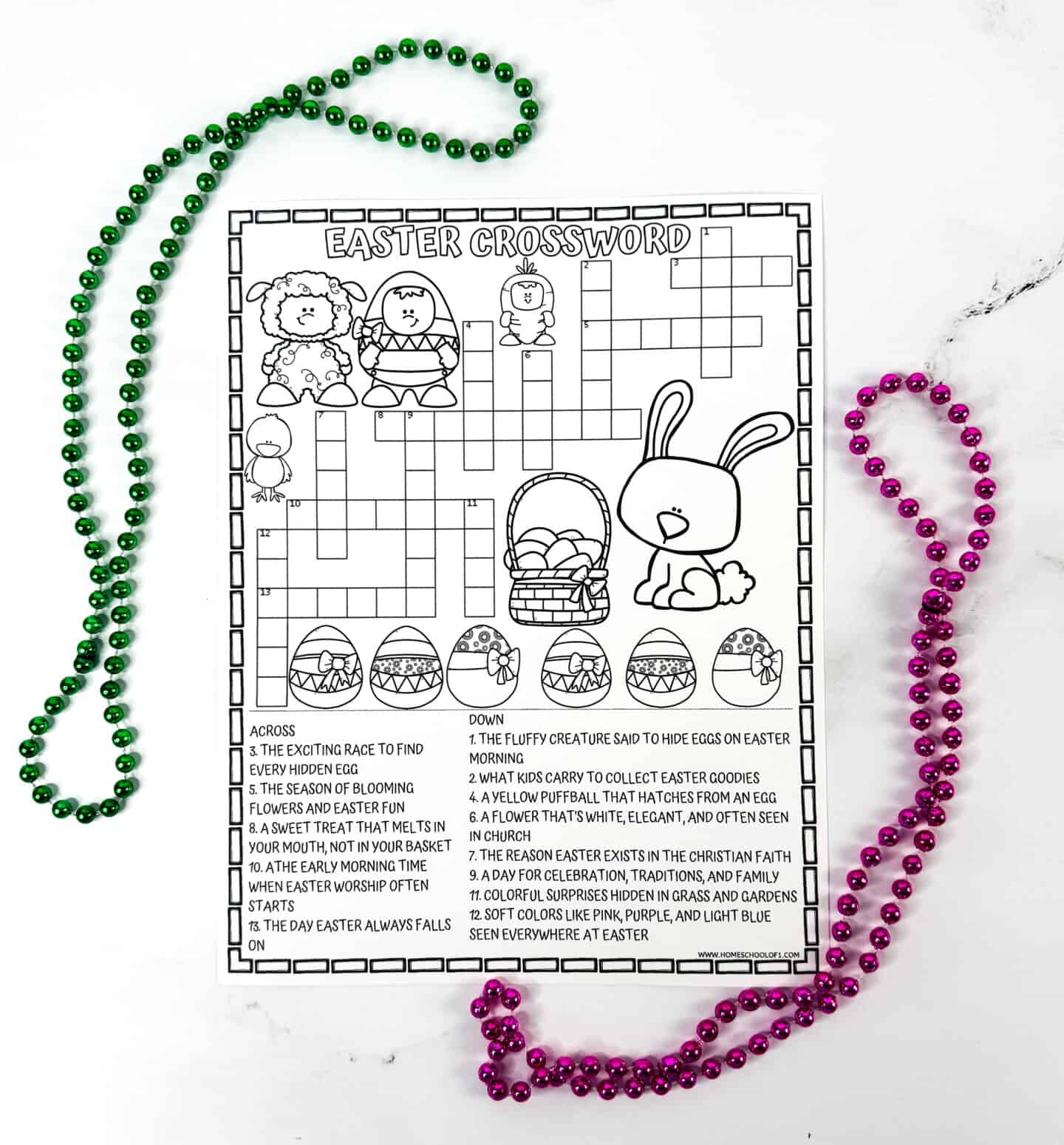 Black and white printable Easter crossword puzzle page featuring outlined illustrations of a bunny, basket, eggs, a lamb, and spring animals. The puzzle clues at the bottom relate to Easter traditions, and the sheet is placed between loops of shiny green and pink beads on a white surface—perfect for coloring.
