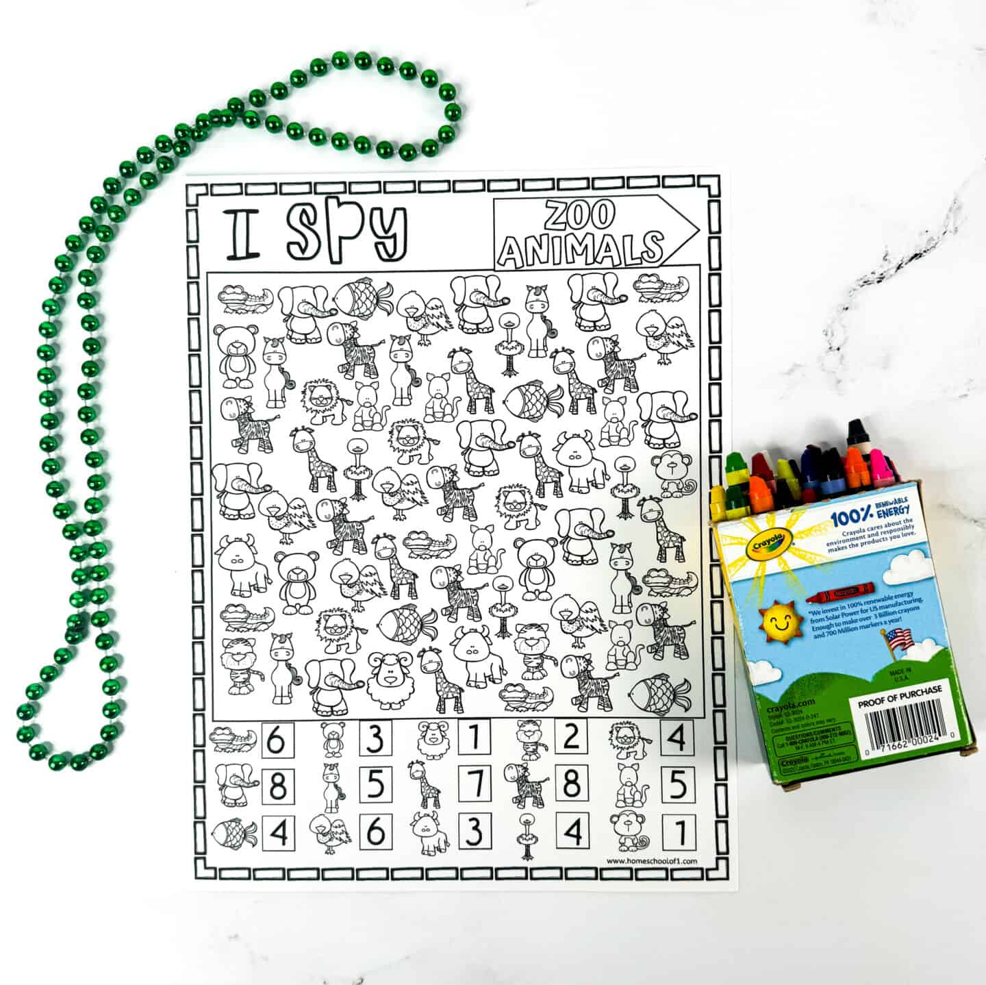 A black and white “I Spy Zoo Animals” printable worksheet featuring cartoon animals such as elephants, lions, giraffes, and crocodiles. The activity sheet includes a counting section at the bottom and is placed on a white surface next to a green beaded necklace and an open box of Crayola crayons, suggesting a fun coloring and counting activity for kids.