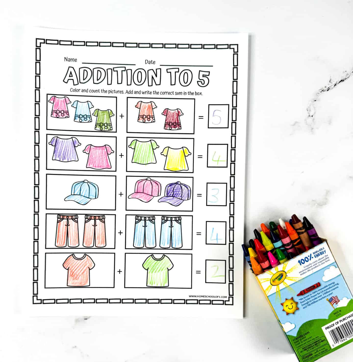 Colored kindergarten addition worksheet with shirts, caps, and jeans, alongside a box of crayons on a white background.