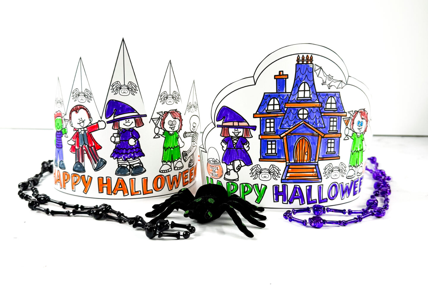 Close-up of two colorful Halloween crowns made from printables, surrounded by purple and black Halloween beads and a black spider decoration.