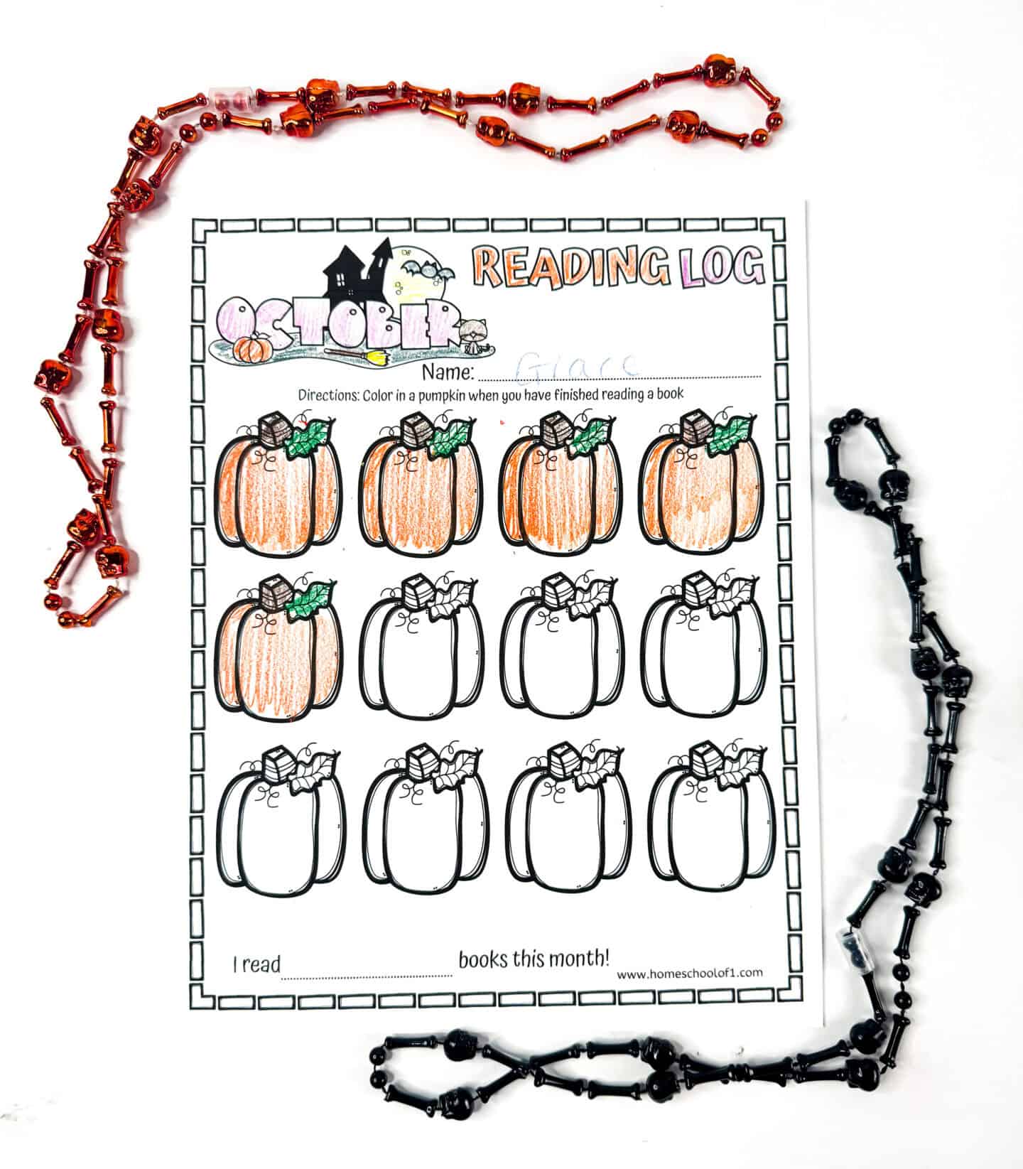 Partially completed October reading log printable with some pumpkins colored orange and green, surrounded by orange and black Halloween bead necklaces.