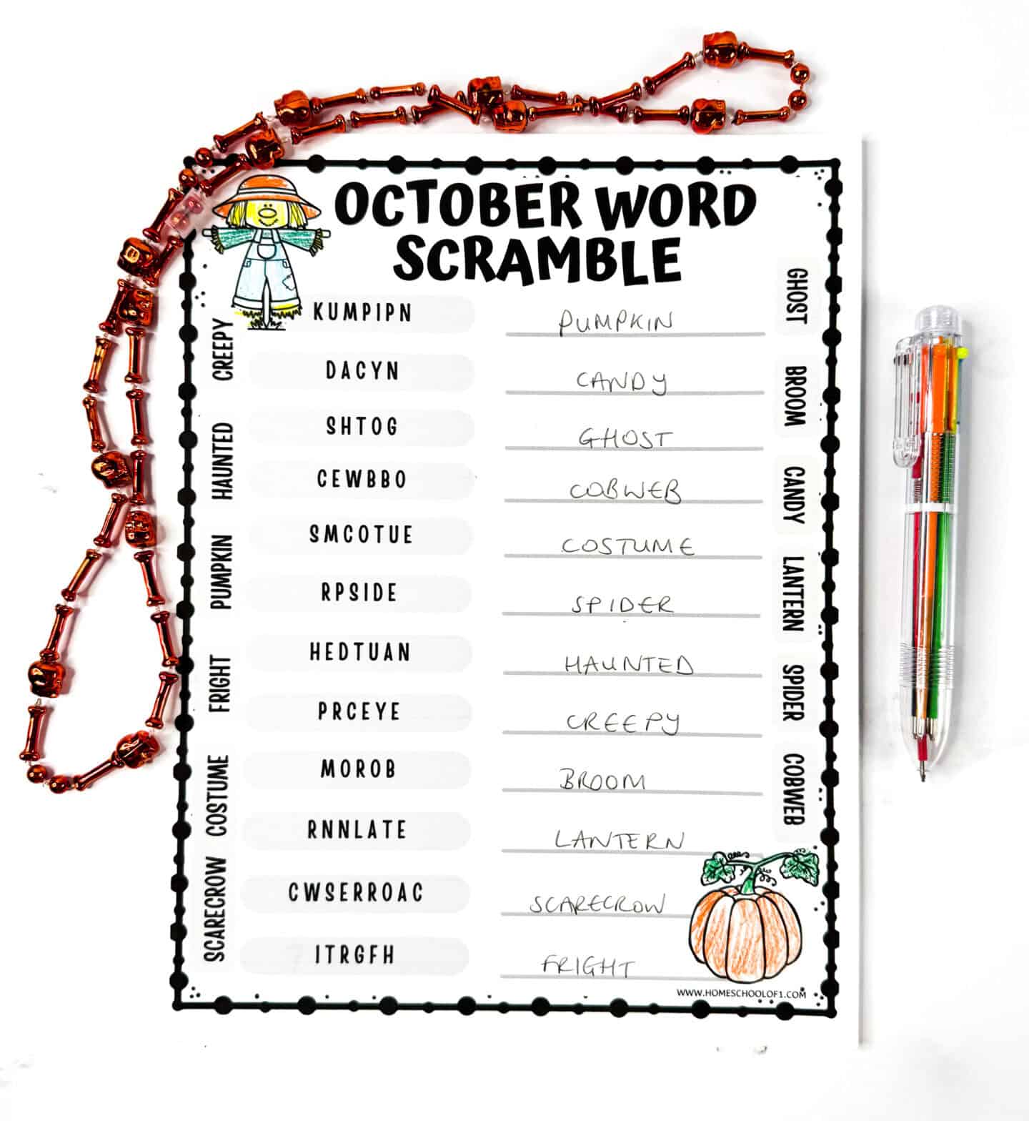 Completed October word scramble worksheet with fall-themed words and handwritten answers, next to colorful pens and Halloween beads.