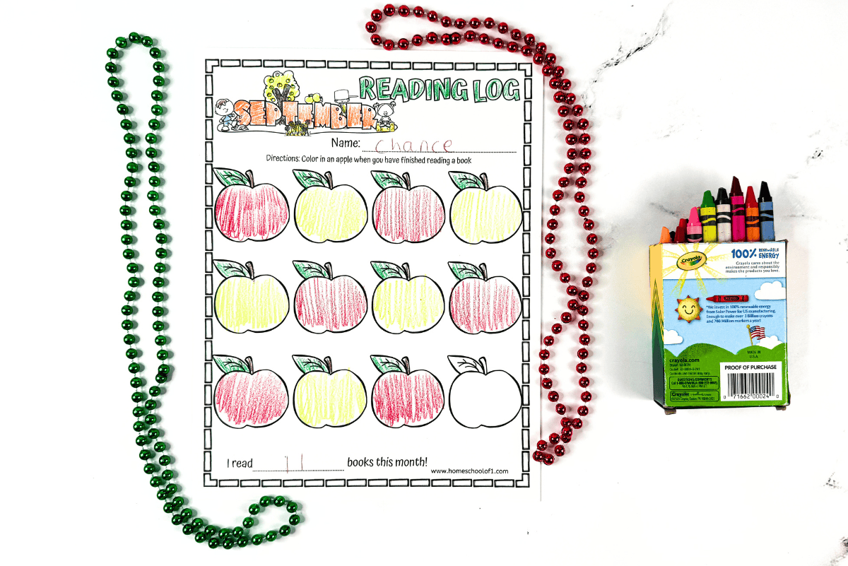 September reading log partially filled in with colored apples, surrounded by red and green beads, crayons nearby.