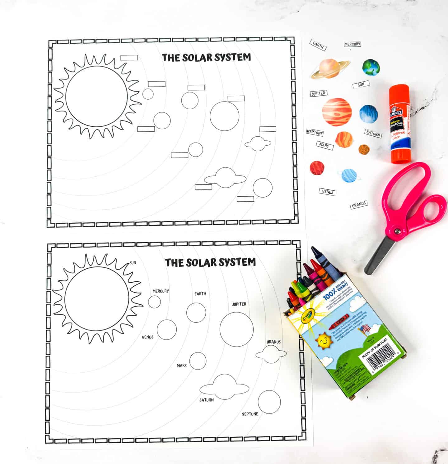 Black-and-white solar system worksheet with planets to label and cut out, crayons, glue stick, and scissors beside it.