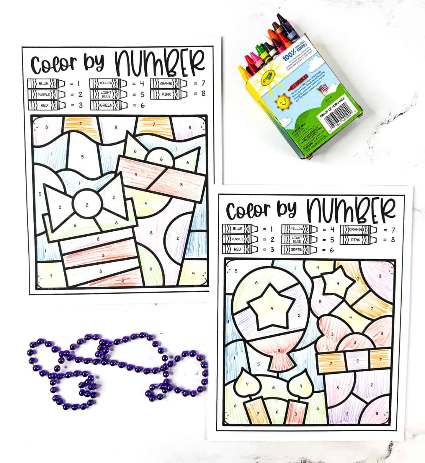 Printable birthday color by number pages with a present and balloon designs, completed with crayons and displayed with purple party beads.