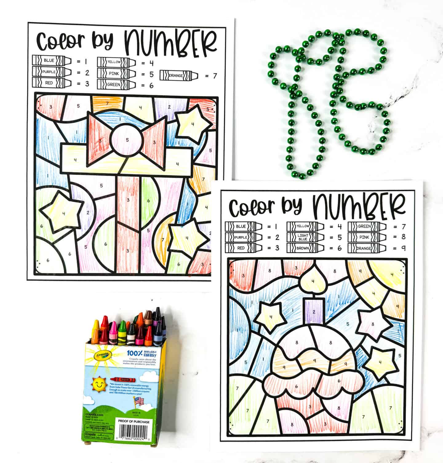Birthday color by number worksheets featuring a gift box and a cupcake with a candle, colored with crayons, shown with green beads.