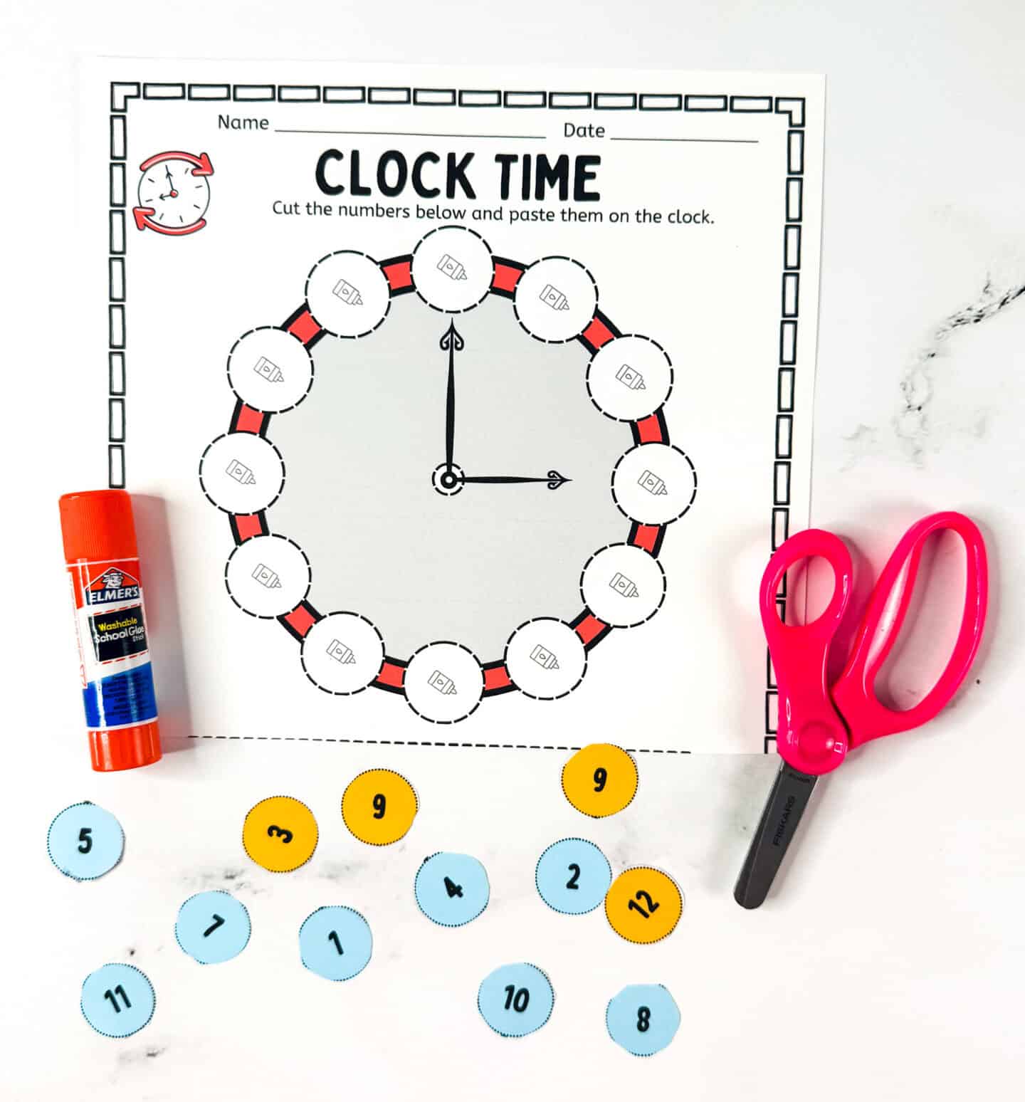 Cut and paste clock worksheet for kids learning to tell time, with glue stick, scissors, and number circles.