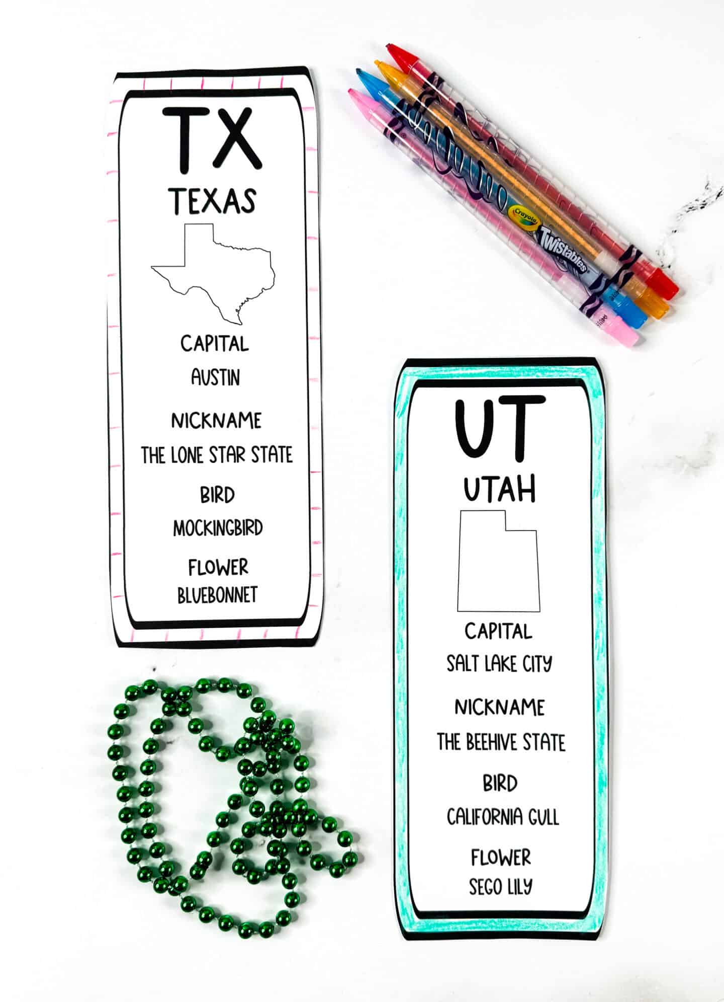 Free printable state bookmarks for Texas and Utah. Texas has a pink striped border and Utah features a teal colored outline. Crayola Twistable pencils and green beads are included in the flat lay.