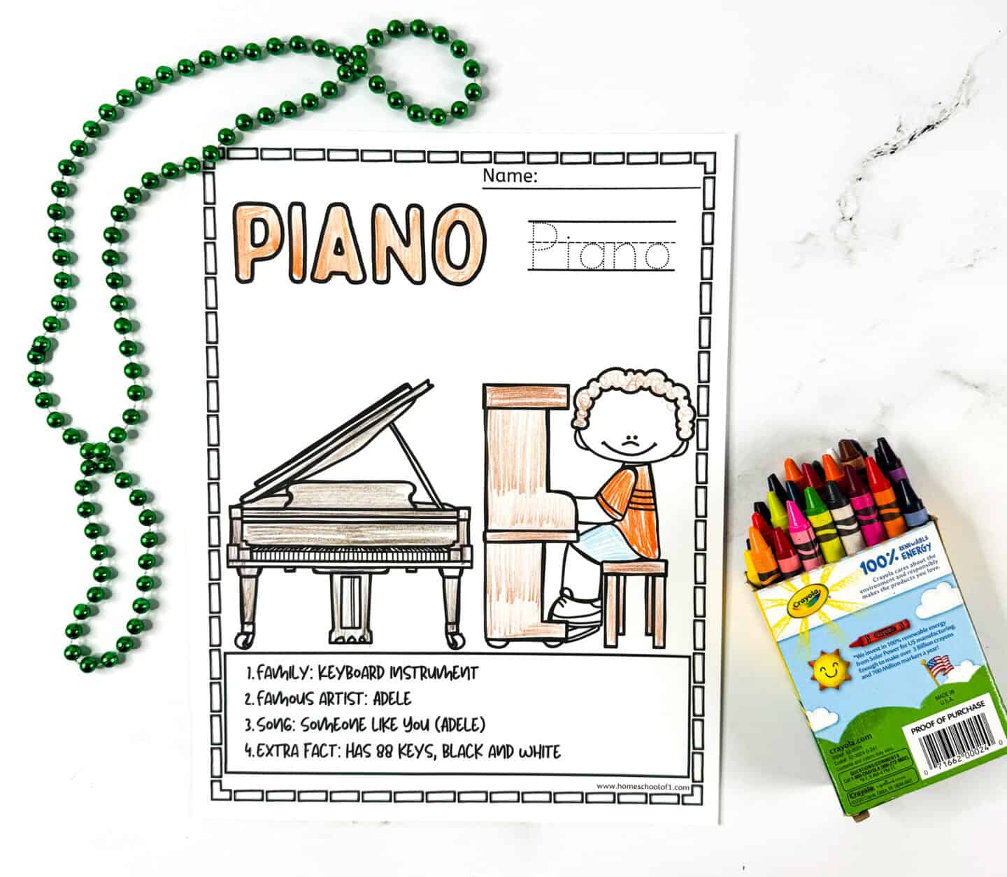 Piano coloring page showing a child at a grand piano with green beads and a box of Crayola crayons on a white background.