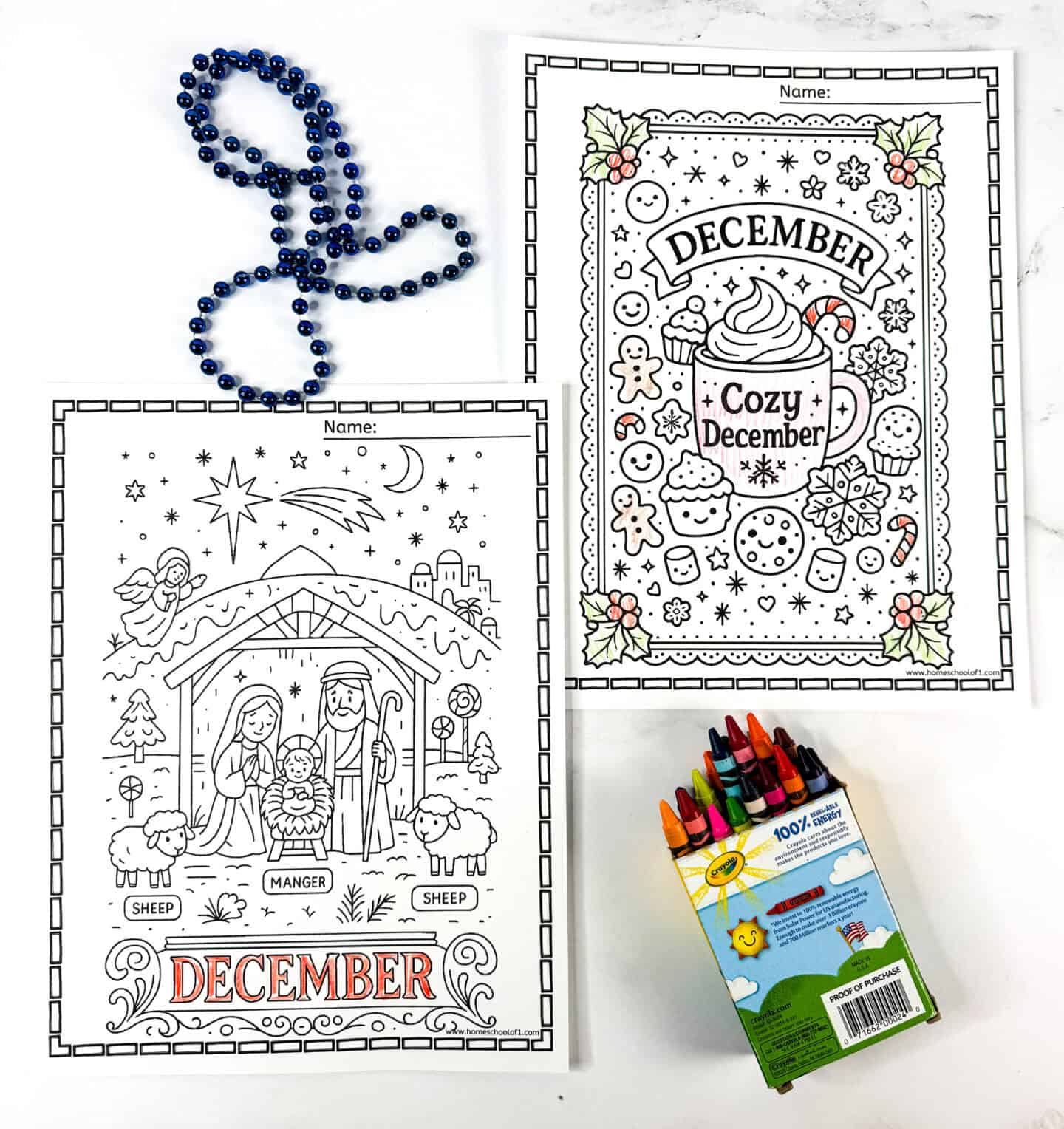 Two December coloring pages, a nativity scene with “December” text and a “Cozy December” mug surrounded by cookies and holiday treats, displayed with crayons and blue beads.