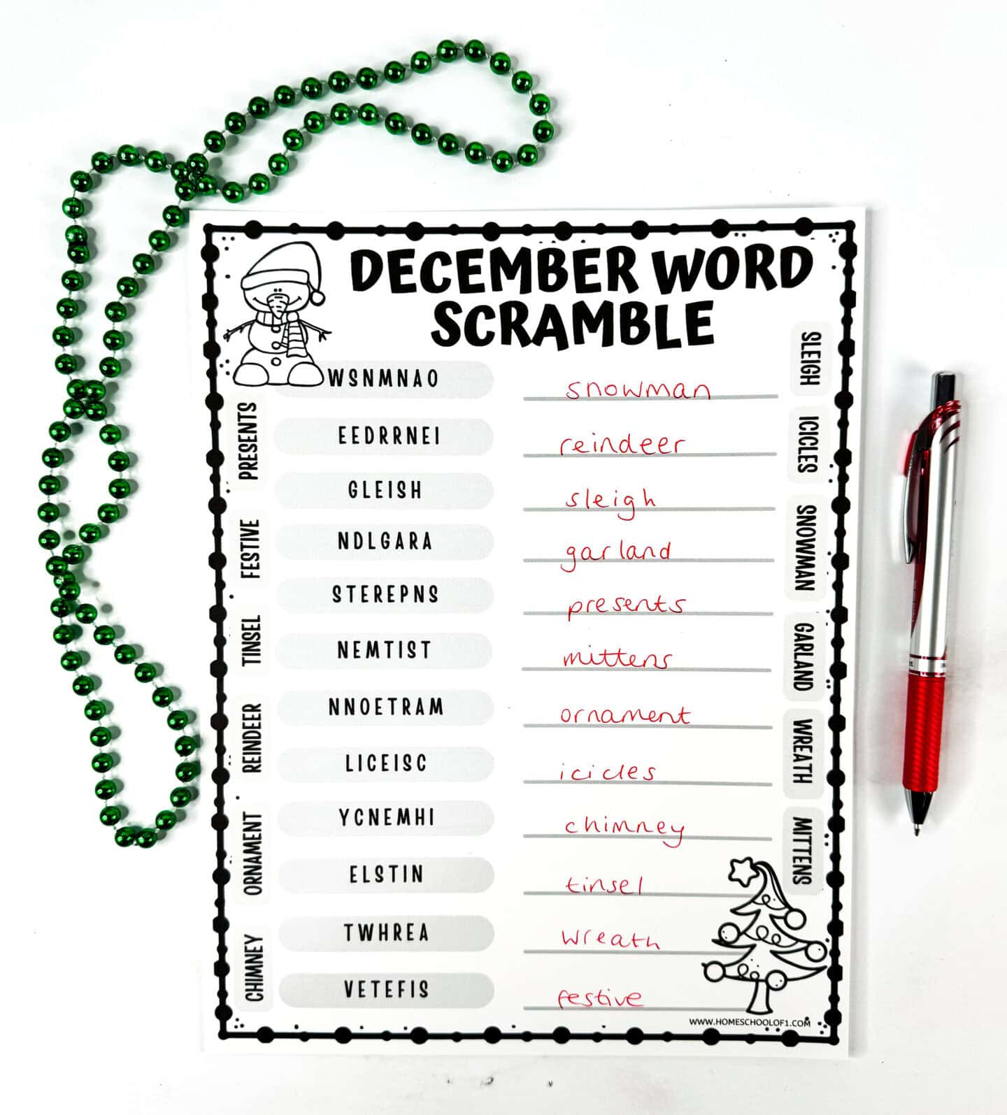 Completed December word scramble worksheet with holiday-themed words written in red ink, green bead garland, and a red pen on the side.